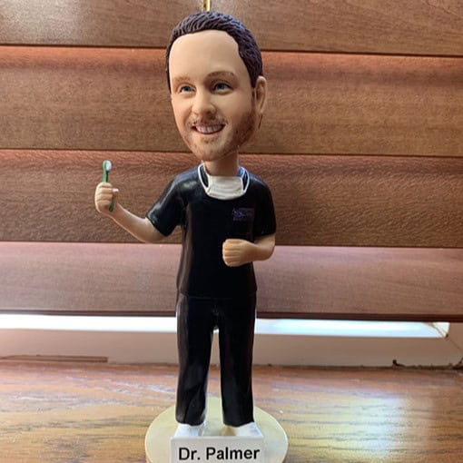 Bobblehead figure of a man labeled 'Dr. Palmer' standing on a base, wearing black scrubs and holding a toothbrush in one hand.